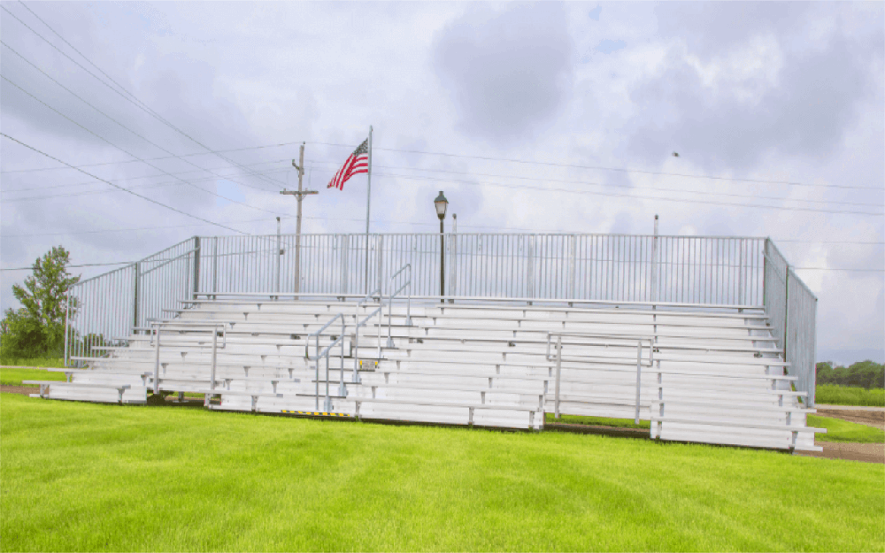 Commercial hydraulic aluminum bleachers fully deployed on grass field, event-ready with guardrails and stair access.